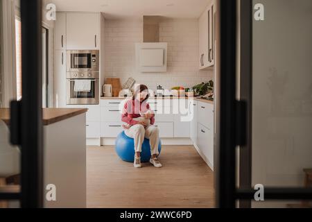 Donna seduta con una bambina su una palla fitness a casa Foto Stock