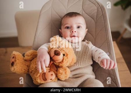 Una bambina adorabile seduta con un giocattolo imbottito sulla sedia rimbalzante Foto Stock
