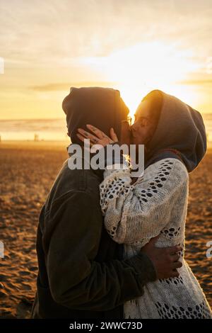 Giovani coppie che si baciano sulla spiaggia al tramonto Foto Stock