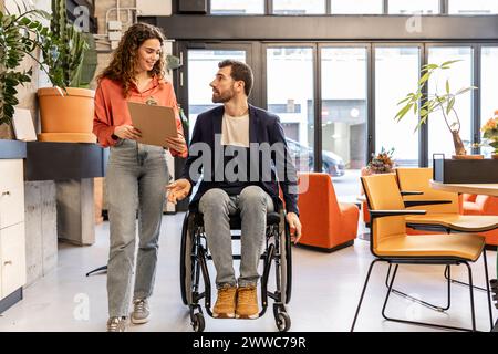 Uomo d'affari in sedia a rotelle che discute con il collega nello spazio di co-working Foto Stock