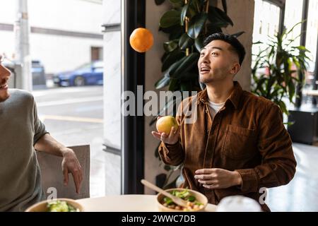 Uomo d'affari che gioca con mela e arancia seduto al bar dell'ufficio Foto Stock