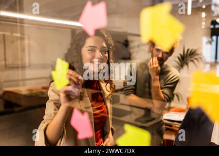 Donna d'affari sorridente dietro un bicchiere con un collega in ufficio Foto Stock