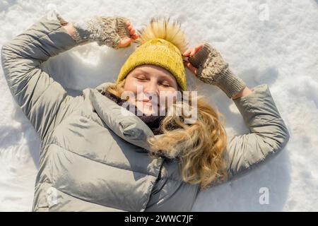 Donna sorridente sdraiata sulla neve con gli occhi chiusi Foto Stock