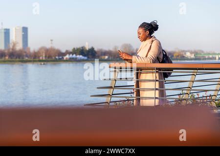 Donna sorridente che usa lo smartphone vicino alle ringhiere Foto Stock