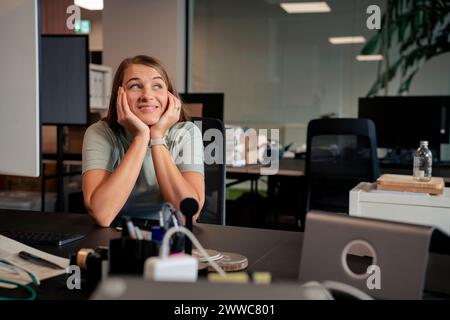 Donna d'affari felice appoggiata ai gomiti alla scrivania in ufficio Foto Stock