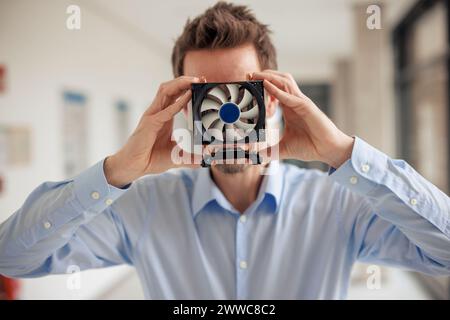 Ingegnere maturo che ricopre la faccia con la ventola della CPU in officina Foto Stock