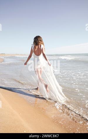 Giovane sposa che indossa un abito da sposa bianco e corre in spiaggia Foto Stock