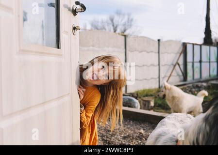 Una ragazza giocosa che si sporge la lingua vicino alla porta nel cortile posteriore Foto Stock