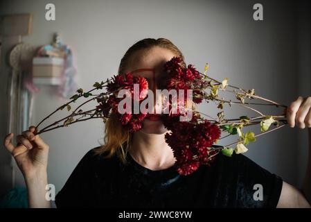 Donna che copre gli occhi con fiori davanti al muro Foto Stock