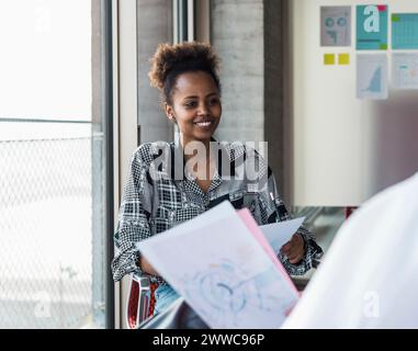 Donna d'affari sorridente con collega che discute di documenti in ufficio Foto Stock