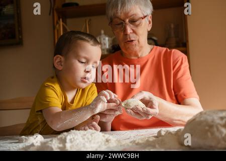 Donna anziana che insegna al nipote a fare panini in cucina a casa Foto Stock