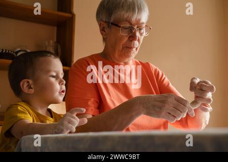 Donna anziana che prepara panini di pasta vicino al nipote in cucina a casa Foto Stock