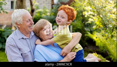 Felice coppia di anziani che si diverte con il nipote in giardino Foto Stock