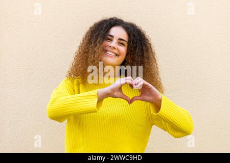 Donna felice che gestiva il cuore con le mani davanti al muro Foto Stock