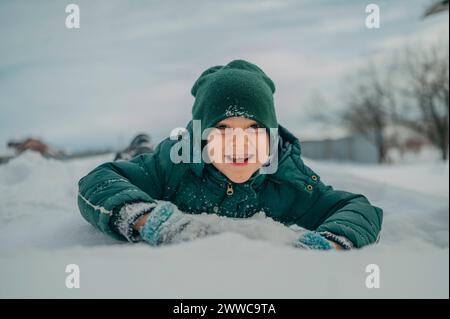 Ragazzo felice sdraiato e che gioca sulla neve Foto Stock