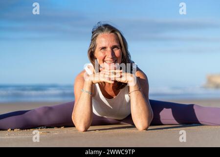 Donna matura felice che pratica yoga in spiaggia Foto Stock