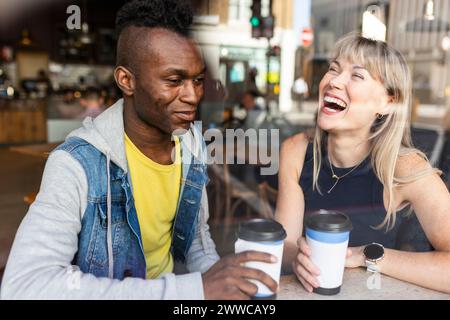 Donna felice seduta con un amico al bar vista attraverso il vetro Foto Stock