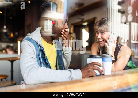 Giovani amici multirazziali che si divertono al bar visto dalla finestra Foto Stock