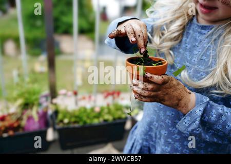 Una ragazza che metteva sporco e fertilizzante in pentola sul balcone Foto Stock