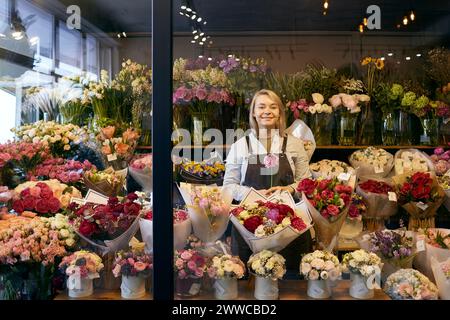 Fiorista sorridente in piedi tra un bouquet di fiori vari al negozio Foto Stock