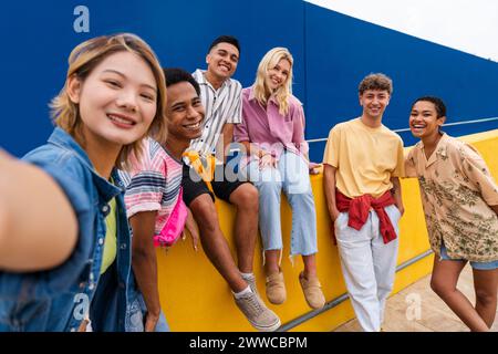 Gruppo di amici amici con abiti colorati seduti sulla parete gialla per scattare foto di gruppo Foto Stock