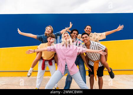 Gruppo di giovani amici con abiti colorati che posa felicemente di fronte al muro Foto Stock
