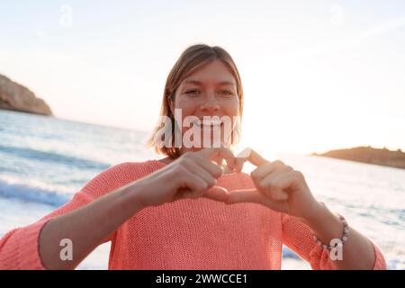 Donna spensierata che gestisce la forma del cuore sulla spiaggia del tramonto Foto Stock