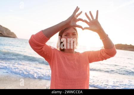 Donna felice che gestiva la forma del cuore sulla spiaggia del tramonto Foto Stock