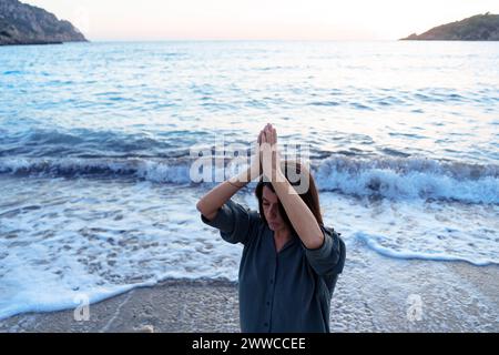 Donna con le mani strette e gli occhi chiusi sulla spiaggia del tramonto Foto Stock