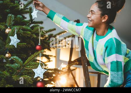 Giovane donna appesa la stella sull'albero di Natale Foto Stock