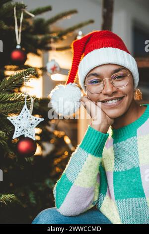 Giovane donna sorridente che indossa il cappello di Babbo Natale a casa Foto Stock