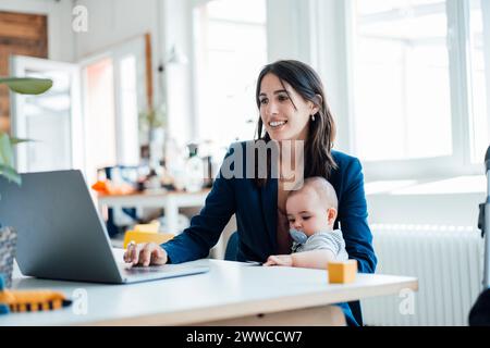 Donna d'affari sorridente seduta con una bambina che usa il laptop a casa Foto Stock