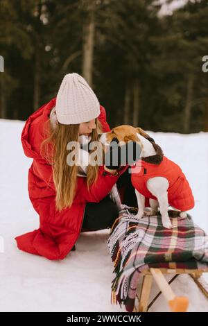 Donna che accarezza il cane seduto su una slitta nella foresta invernale Foto Stock