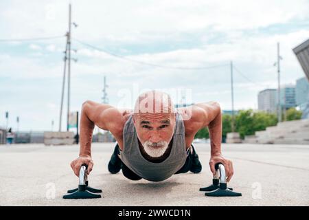 Uomo anziano attivo che fa push-up sulle maniglie Foto Stock