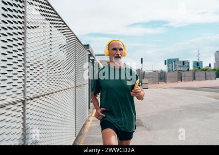 Uomo anziano attivo che ascolta musica e fa jogging per recinzione Foto Stock