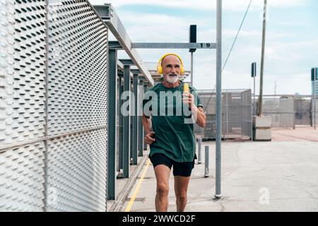 Uomo anziano che ascolta musica e fa jogging per recinzione Foto Stock