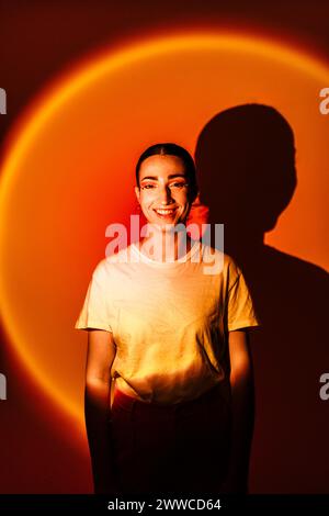 Giovane donna felice in piedi con illuminazione al neon su sfondo arancione Foto Stock