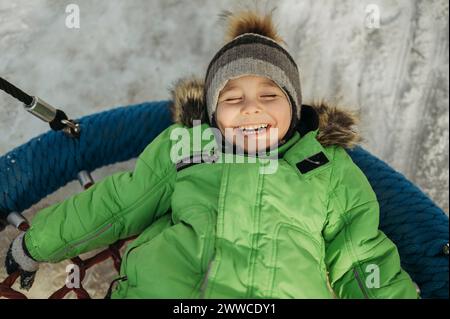 Ragazzo spensierato sdraiato sull'altalena in inverno al parco Foto Stock