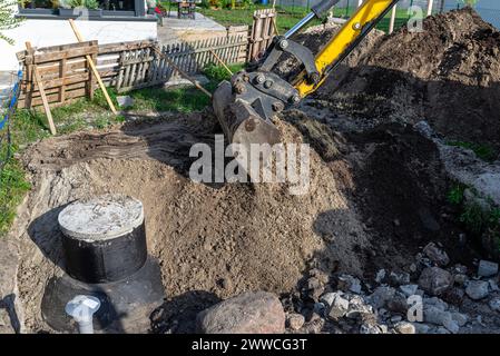 Utilizzo di un escavatore per seppellire un serbatoio settico in cemento da 10 m3 situato nel giardino accanto alla casa. Foto Stock