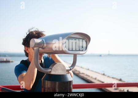 l'uomo guarda attraverso un binocolo stazionario. Binoscopio sulla piattaforma di osservazione vicino al mare. porto marittimo di Odessa. Yacht costosi sul molo. Machi commerciali Foto Stock