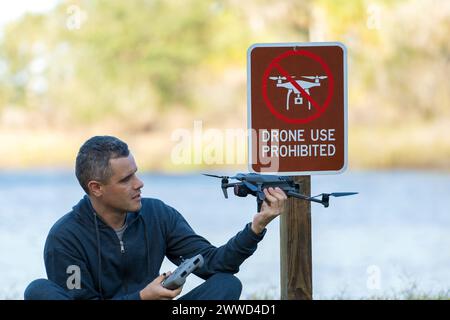 L'uomo volerà il suo quadricottero in nessuna zona di droni. L'operatore utilizza illegalmente il proprio UAS nel parco statale vicino al segnale di restrizione Foto Stock