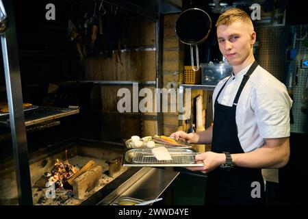 Chef maschio che tiene in mano filetto di luccio con verdure su vassoio di rete di ferro prima di friggere Foto Stock