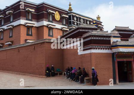 Pellegrini che si riposano su una panchina accanto a uno dei templi del monastero di Labrang, contea di Xiahe, prefettura autonoma tibetana di Gannan, Gansu, Cina Foto Stock