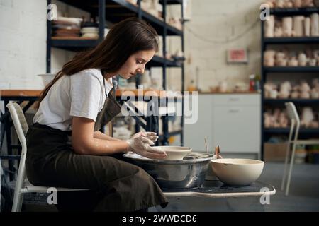 donna potter che crea un vaso di terra su una ruota di ceramica in officina Foto Stock