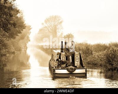 La coppia e il loro cane navigano in barca sul canale Trent e Mersey, Inghilterra, Regno Unito, Gran Bretagna vicino ad Alrewas, Staffordshire Foto Stock