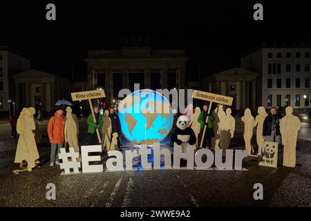 Berlino, Internazionale. 23 marzo 2024. I membri dell'organizzazione per la protezione dell'ambiente World Wide Fund for Nature (WWF) partecipano alla campagna globale "Earth Hour" e si trovano di fronte alla porta di Brandeburgo non illuminata. Con "ora della Terra", l'organizzazione per la protezione ambientale World Wide Fund for Nature (WWF) vuole dare l'esempio per la protezione del clima e dell'ambiente. Il motto di quest'anno è: "La tua ora per la Terra!". Credito: Joerg Carstensen/dpa/Alamy Live News Foto Stock