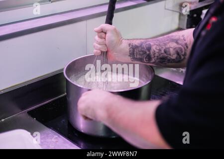 primo piano delle mani di uno chef che sbattono il contenuto di una pentola nella sua cucina, mostrando il processo di preparazione del cibo e l'attenzione ai dettagli nel gattino Foto Stock