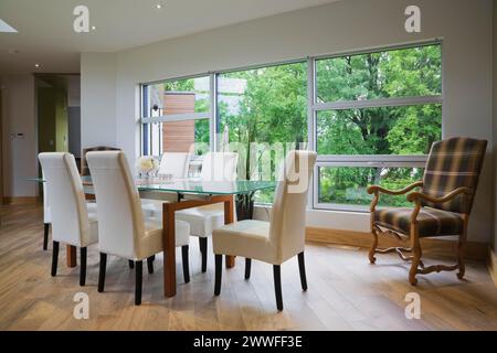 Tavolo con piano in vetro trasparente e sedie con schienale alto in pelle bianca nella sala da pranzo con pavimento in piastrelle di ceramica beige all'interno di una casa moderna in stile cubista, Quebec, Canada Foto Stock