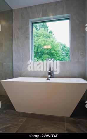 Vasca da bagno bianca a forma di vaso indipendente nel bagno con pavimento in piastrelle di ceramica grigia e pareti al piano terra all'interno di una casa moderna in stile cubista, Quebec Foto Stock