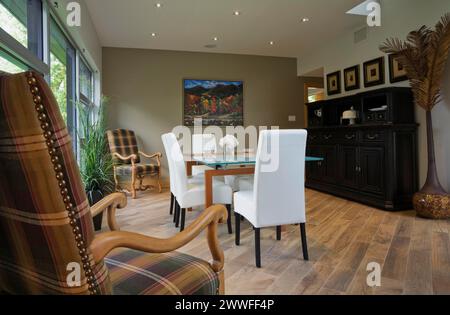 Tavolo con piano in vetro trasparente e sedie con schienale alto in pelle bianca nella sala da pranzo con pavimento in piastrelle di ceramica beige all'interno di una casa moderna in stile cubista, Quebec, Canada Foto Stock